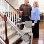 Couple standing beside the Bruno Elan stair lift at the bottom of their staircase