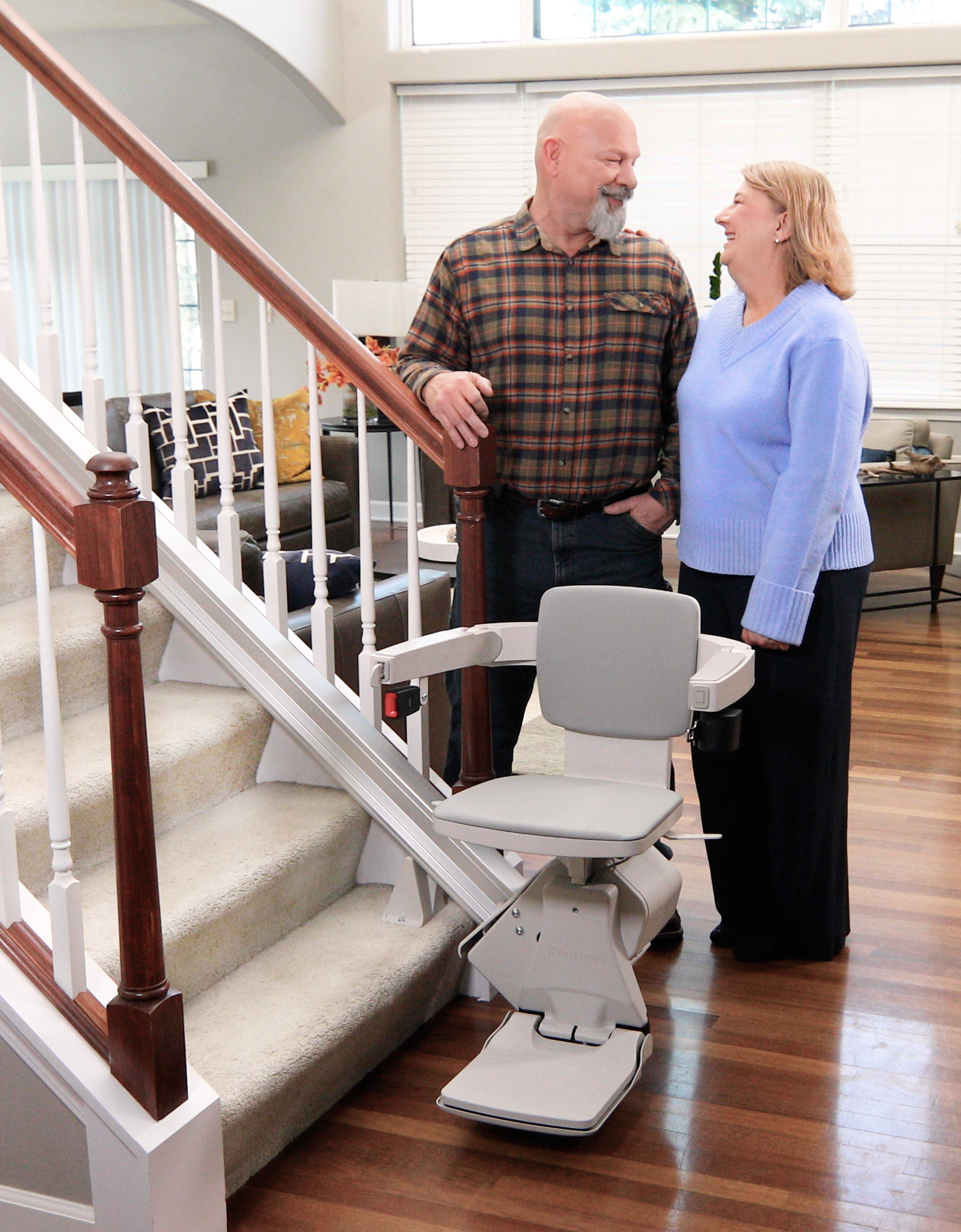 Couple standing beside the Bruno Elan stair lift at the bottom of their staircase