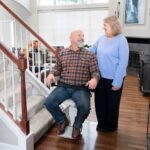 Couple and their dog standing beside the Bruno Elan stair lift at the bottom of the staircase