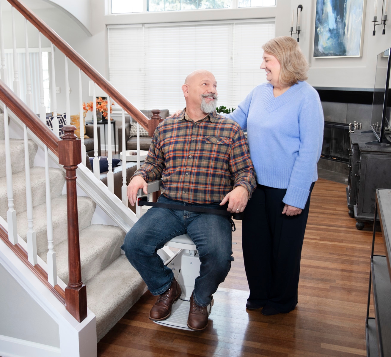 Couple and their dog standing beside the Bruno Elan stair lift at the bottom of the staircase
