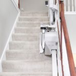 View down a carpeted staircase with the Bruno Elan stair lift folded at the bottom