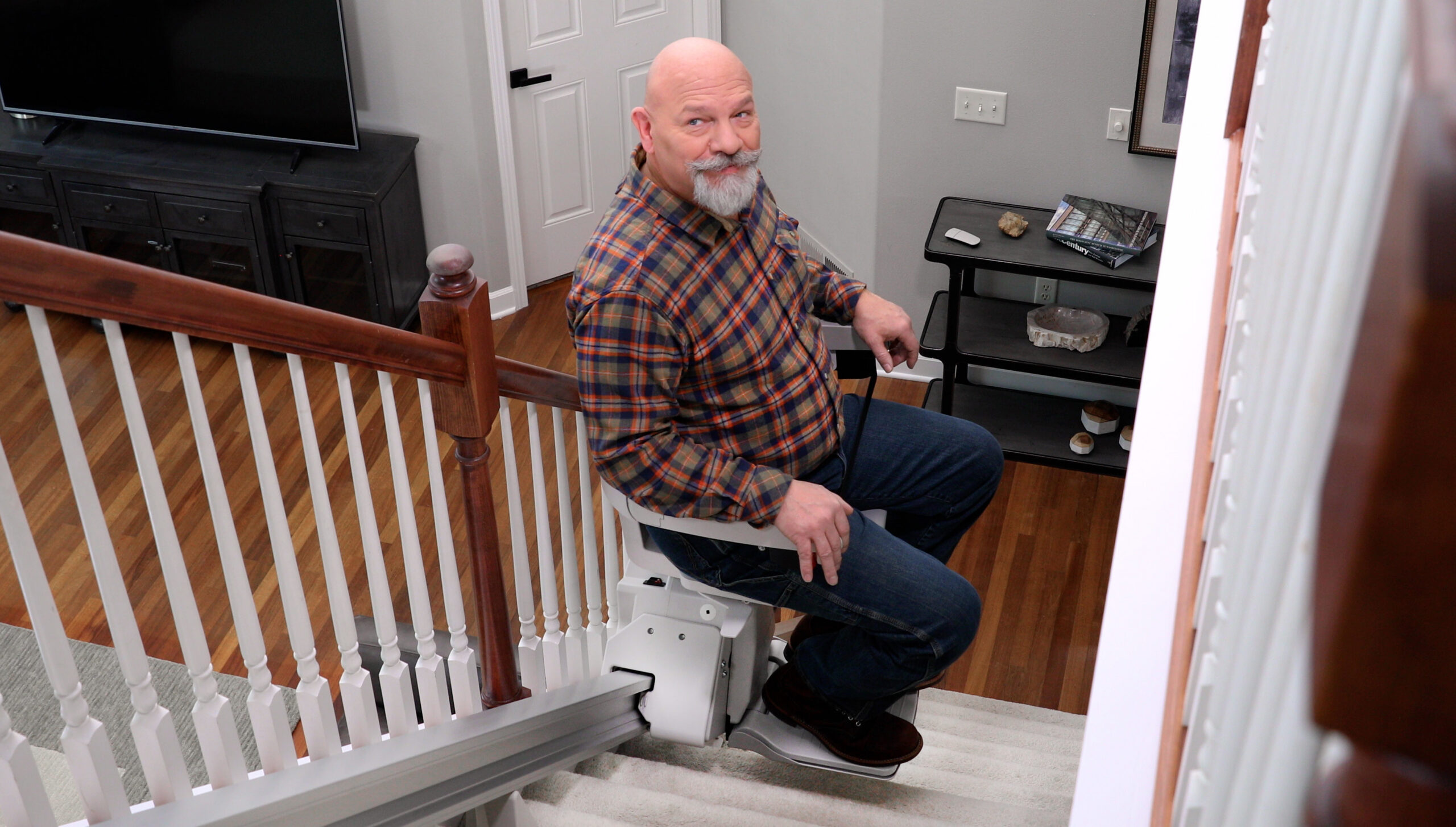Man seated on the Bruno Elan stair lift at the bottom of the stairs, using the hand control