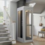 Harmar Spire Home Elevator with a light grey frame and glass door beside a staircase in a bright entryway